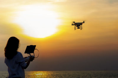 Woman flying drone over sea against sky during sunset