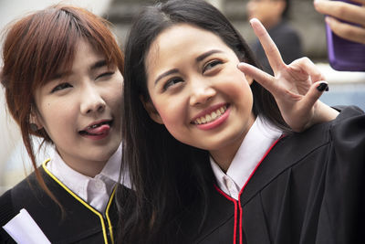 Close-up of cheerful female students wearing graduation gowns while taking selfie with mobile phone