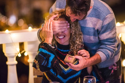 Smiling man closing eyes of woman from behind at night