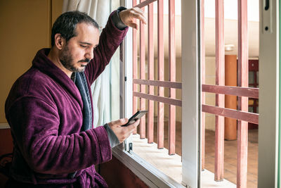 Man using phone while standing by window at home