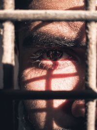 Close-up portrait of young man looking through metal grate