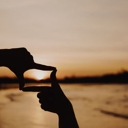 Silhouette hand holding sea against sky during sunset