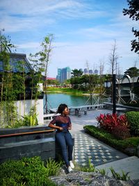 Black woman sitting on a ledge in a little chinese garden, with a lake in the background. 