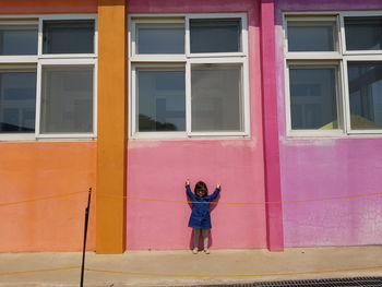 Full length of woman standing by pink building
