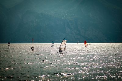 People enjoying windsurfing in sea against mountain