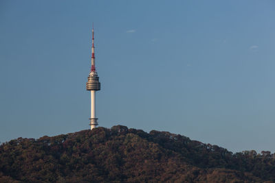 Low angle view of communications tower on hill against blue sky