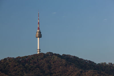 Low angle view of communications tower on hill against clear blue sky