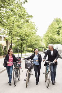 Full length of business people with bicycles walking on street