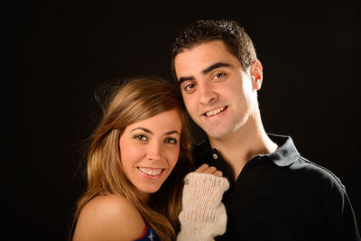Portrait of couple smiling while standing against black background