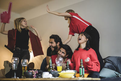 Happy male and female fans celebrating while watching soccer match at home