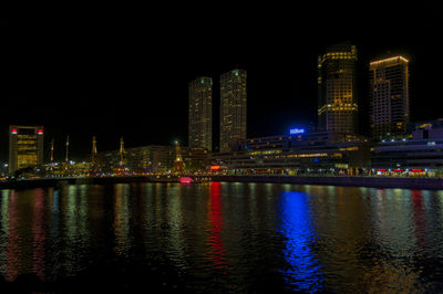 Illuminated buildings by river against sky at night