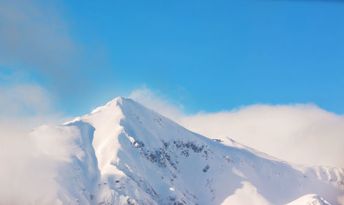 Low angle view of snowcapped mountains against blue sky