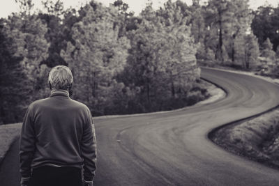 Rear view of senior man standing on road against trees in forest