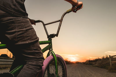 Midsection of man riding bicycle against sky during sunset