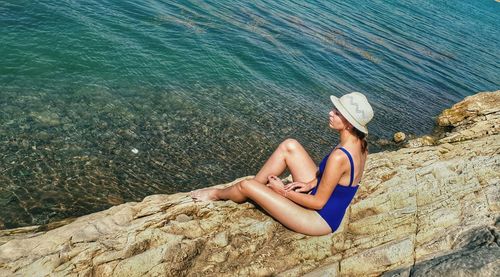 High angle view of woman in bikini sitting on log at beach