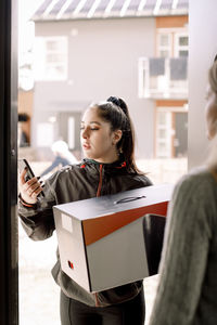 Delivery young woman using mobile phone while delivering package to customer