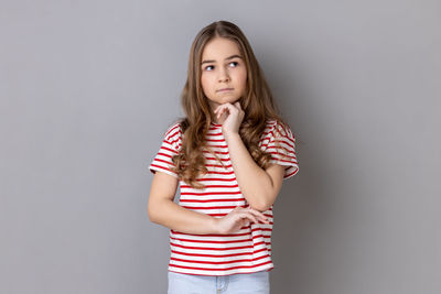 Portrait of young woman standing against gray background