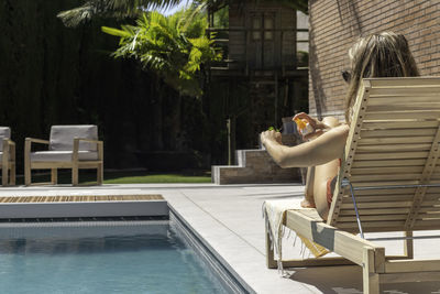 Unrecorgnizable young blonde woman putting sun cream on arm while sun bathing in the swimming pool