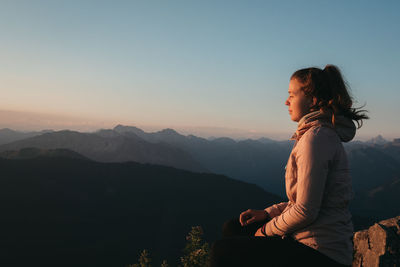 Woman sitting on mountain against sky during sunrise 