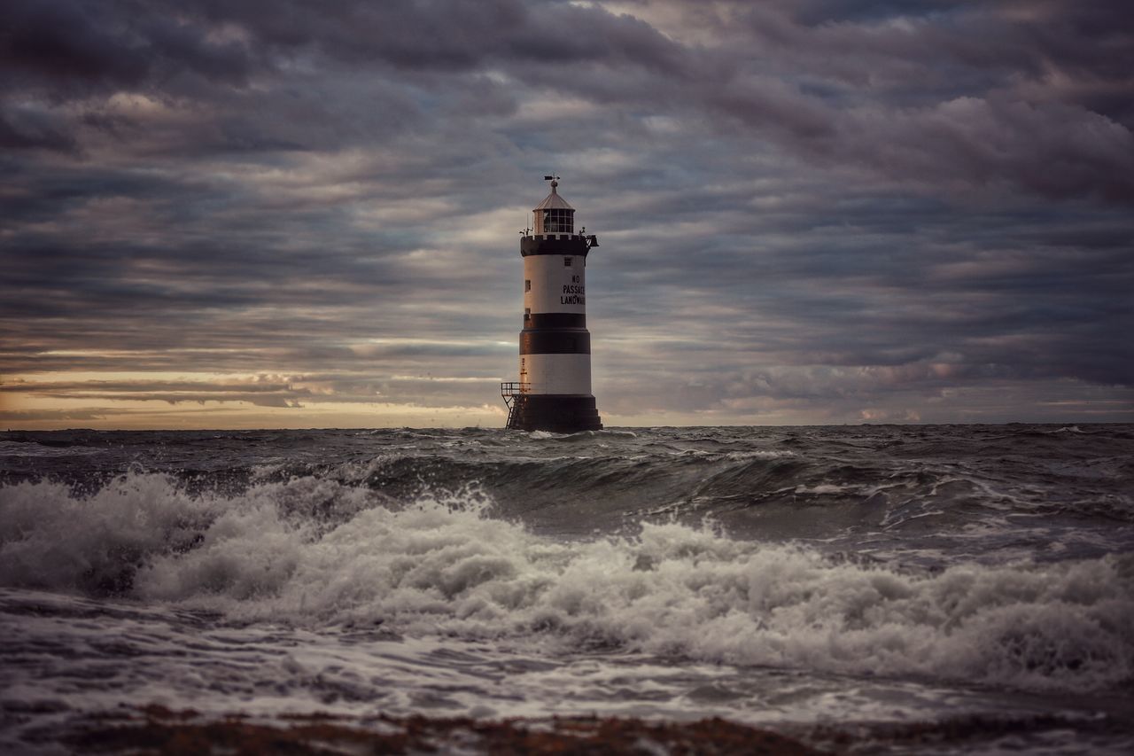 LIGHTHOUSE AMIDST SEA AND BUILDINGS AGAINST SKY