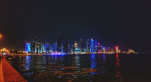 Illuminated city by river against sky at night