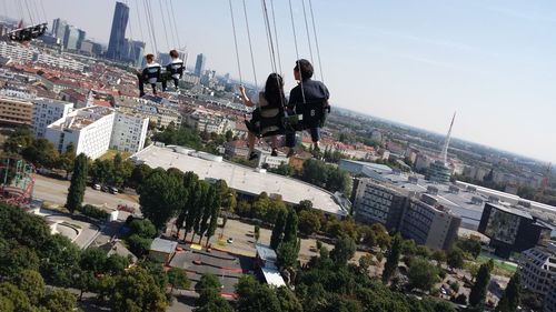 People on chain swing ride over buildings in city