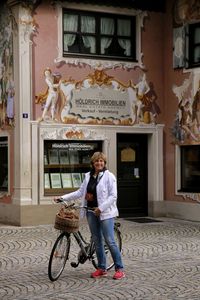 Full length portrait of woman with bicycle standing against building