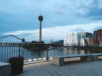 Rheinturm tower by rhine river in city against cloudy sky