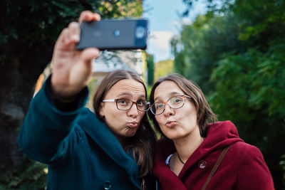 Smiling twins puckering while taking selfie with smart phone