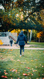 Rear view of woman walking on autumn leaves in park