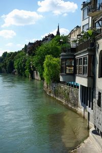 View of buildings by river against cloudy sky