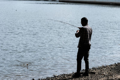 Rear view of man fishing at lakeshore