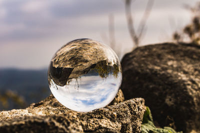 Close-up of crystal ball on rock against sky