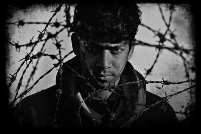 Portrait of man looking through barbed wire fence