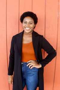 Portrait of a smiling young woman standing against wall