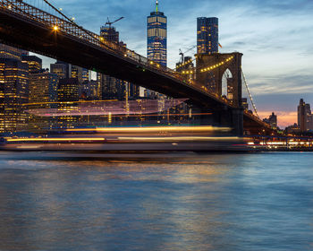 Illuminated bridge over river against sky in city at dusk