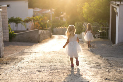 Two girls in white dresses running down a street filled with golden light