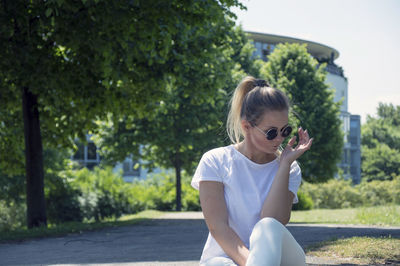 Happy young woman holding sunglasses against trees