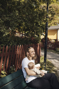 Man feeding milk to toddler daughter while sitting on bench