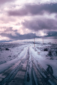 Snow covered road against cloudy sky during sunset