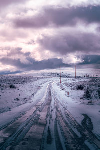 Snow covered road against sky during sunset