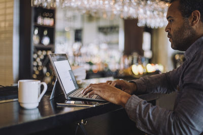 Side view of male entrepreneur using laptop at bar counter in restaurant