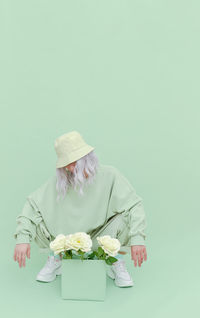 Full length of woman crouching by flowers in box over green background