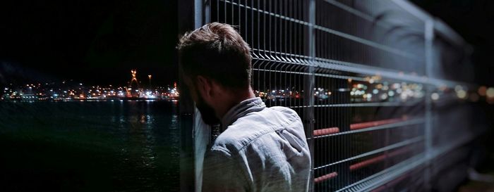 Panoramic view of man standing by metallic fence on pier at night