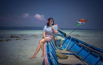 Young woman sitting on boat against sky