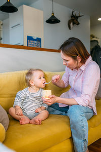 Mom feeds a small child at home with yogurt from a spoon. family concept