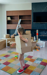 Full length of boy with cardboard box standing on carpet at home