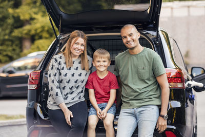 Portrait of happy family sitting in car trunk at back yard