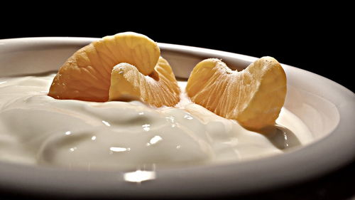 Close-up of oranges and cream in bowl against black background