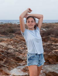 Teenage girl standing with heads over head on cliff by the sea at sunset 